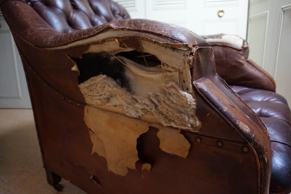 Close-up van de achterzijde van een bruin leren fauteuil met een grote scheur in de bekleding
