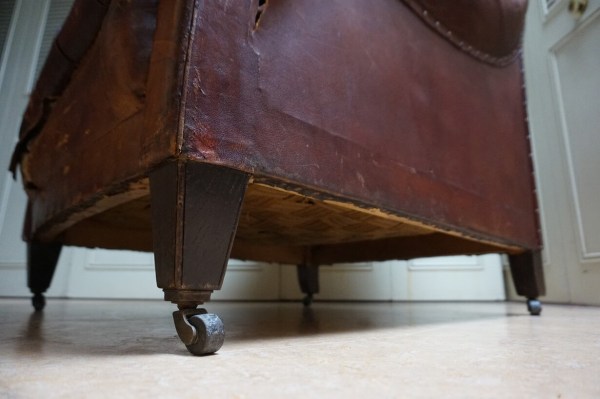 Low angle front view showing a torn lower leather panel on an antique armchair