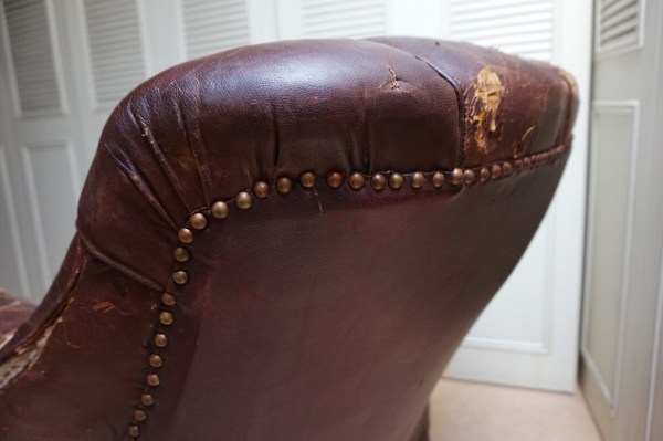 Main soulevant le cuir déchiré de l'accoudoir d'un fauteuil club vintage à restaurer