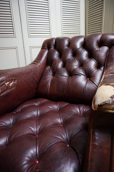 Dettaglio ravvicinato dell'accoudoir logorato e graffiato di una poltrona Chesterfield usata