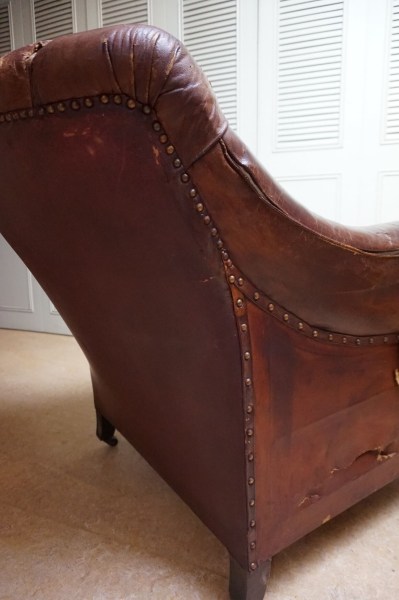 Angled rear view of a vintage brown leather Chesterfield armchair with brass casters