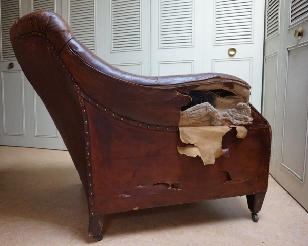 Schrägansicht eines alten Chesterfield Sessels aus braunem Leder mit starken Gebrauchsspuren