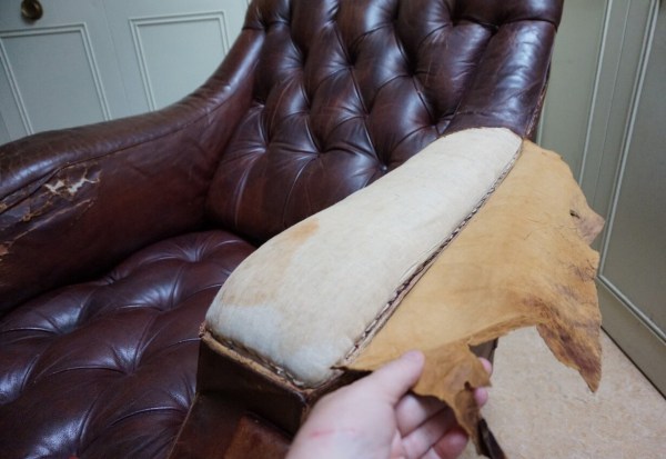 Close-up of worn distressed leather and exposed padding on a vintage Chesterfield armchair